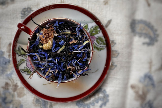 Teacup full of black tea leaves and bright blue flowers