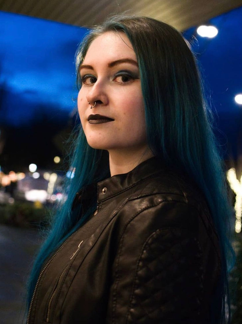 A blue-haired goth human in a black leather jacket smiles at the camera.