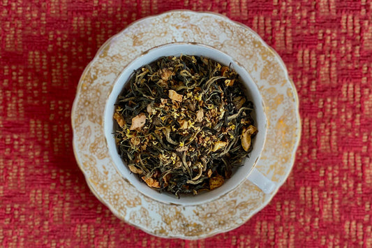 teacup full of gold-tipped black tea leaves with citrus peel and osmanthus flowers