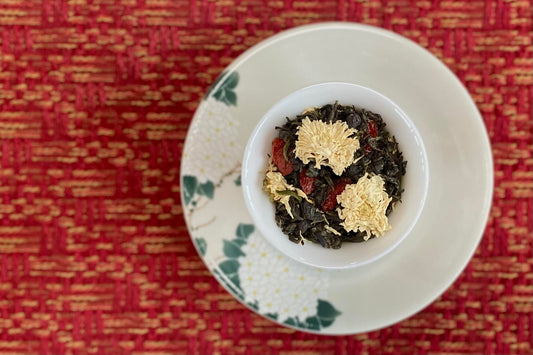 Teacup full of green tea, goji berry, and white chrysanthemum flowers