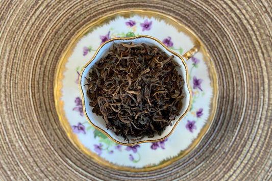 teacup full of brown-tipped black tea leaves