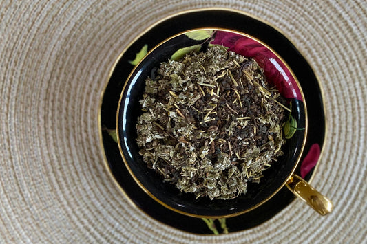 teacup full of dark tea leaf, raspberry leaf, and rosemary