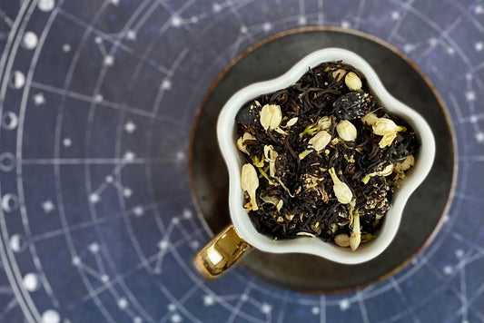 teacup full of black tea, blueberries, and white flowers
