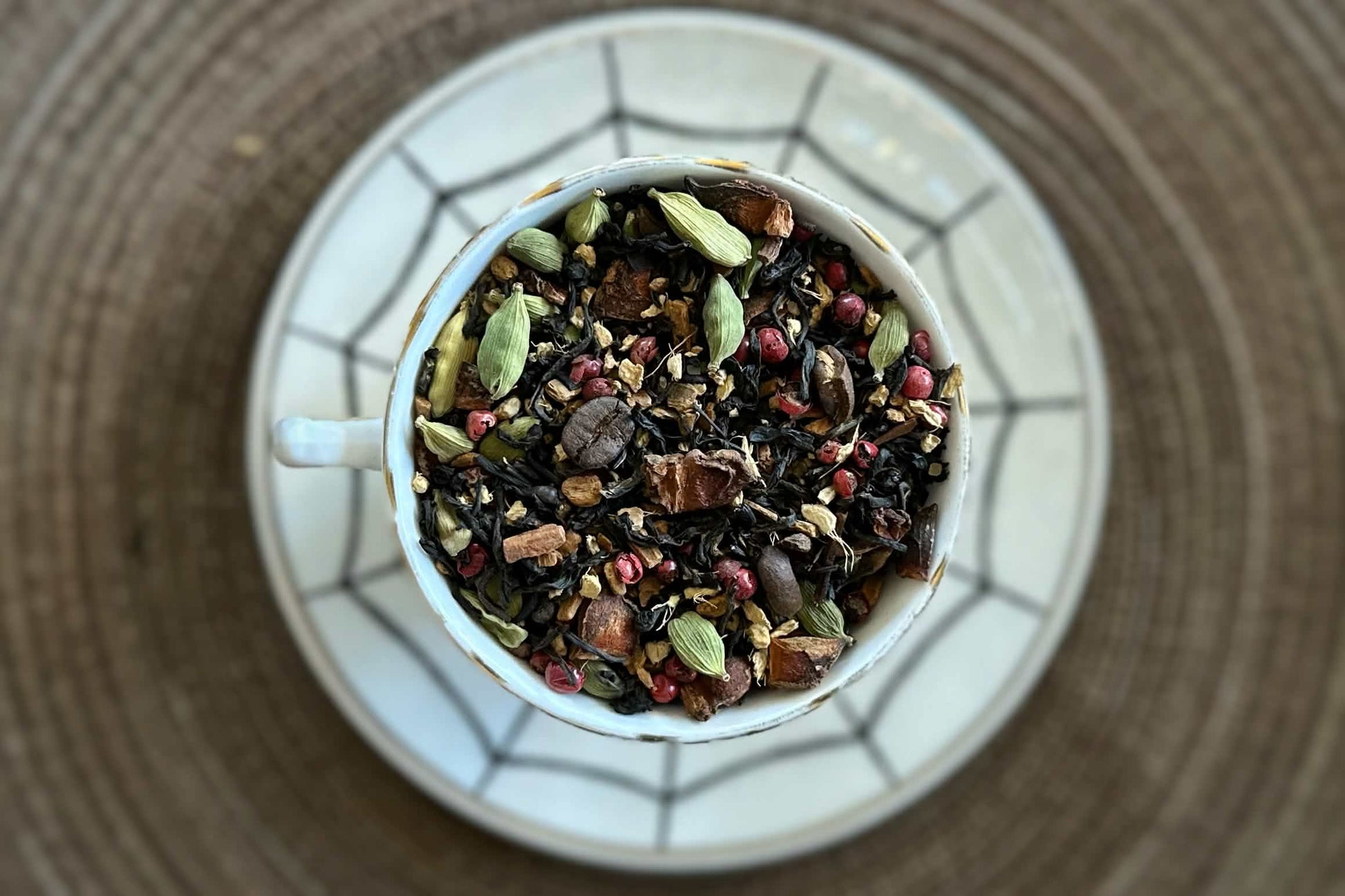 Teacup full of black tea with chai spices and coffee beans on a spiderweb saucer 
