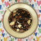 A teacup full of spices, chocolate, almonds and black tea on a colorful heart background