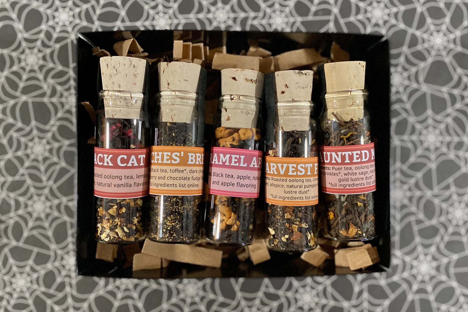 Set of tea samples in small glass jars with labels on a patterned background
