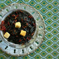Teacup full of deep green tea with chunks of mango and feathery red safflower petals