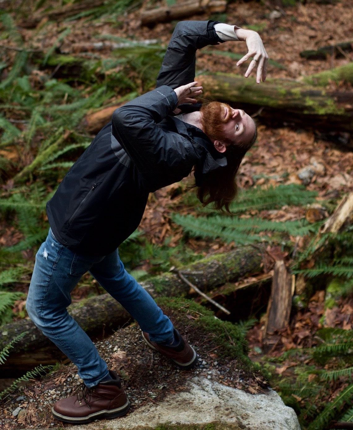 A red-bearded human bends over backward in the woods.