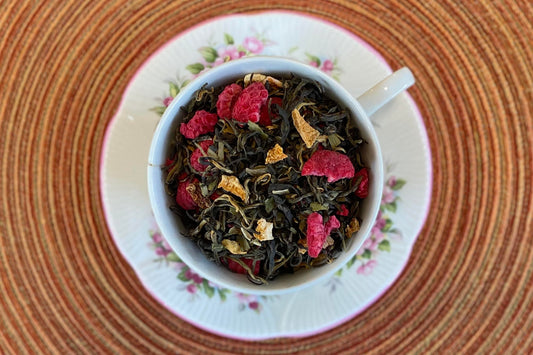 teacup full of dark green tea leaves, raspberry pieces and lemon peel