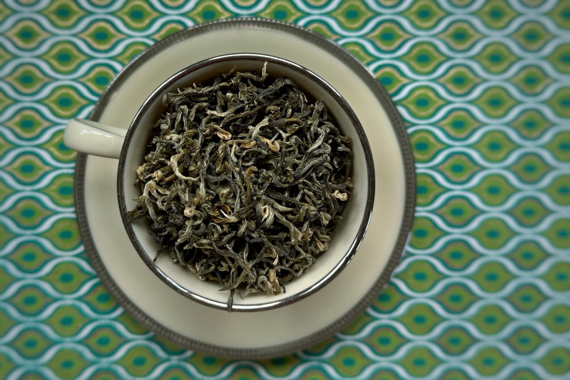 Tea leaves in a white teacup with a green geometric patterned background