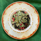 Teacup full of cut green and black leaves with pink peppercorn and tiny yellow flowers