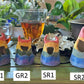 Four grinning horned blob tea pets with rainbow stripes over their whole bodies numbered GR1, R2, SR1, SR2