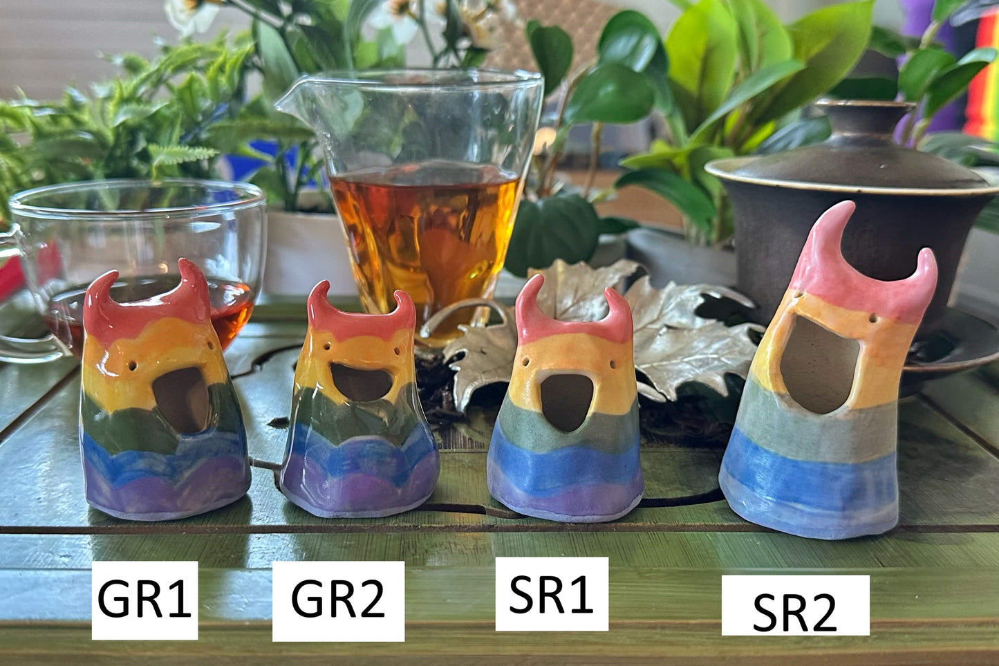 Four grinning horned blob tea pets with rainbow stripes over their whole bodies numbered GR1, R2, SR1, SR2
