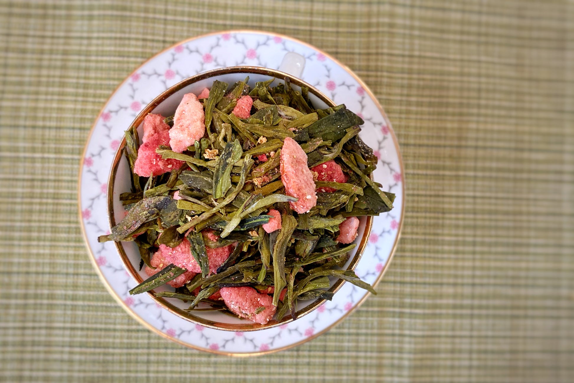 A pink and white teacup holds glitter-dusted green tea leaves and strawberries.